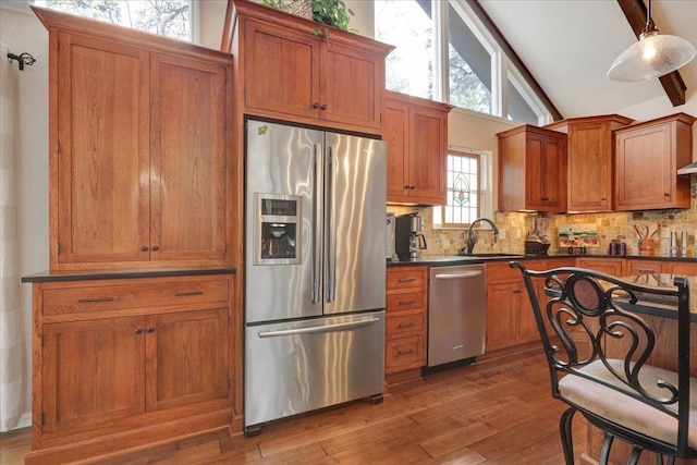 kitchen featuring a sink, dark countertops, stainless steel appliances, brown cabinetry, and vaulted ceiling