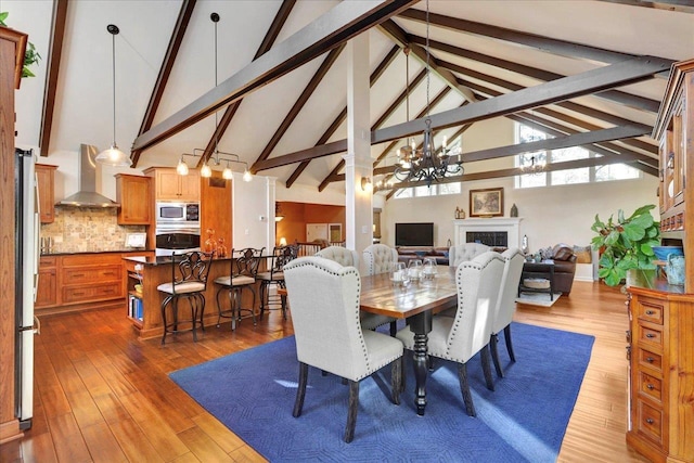 dining space featuring beam ceiling, high vaulted ceiling, hardwood / wood-style flooring, an inviting chandelier, and a fireplace