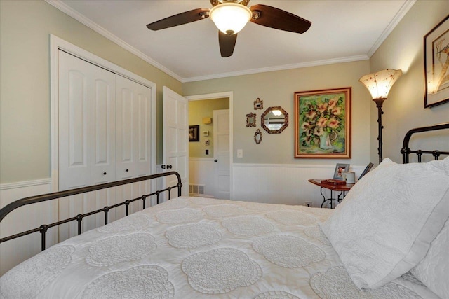 bedroom featuring a ceiling fan, visible vents, a wainscoted wall, a closet, and crown molding