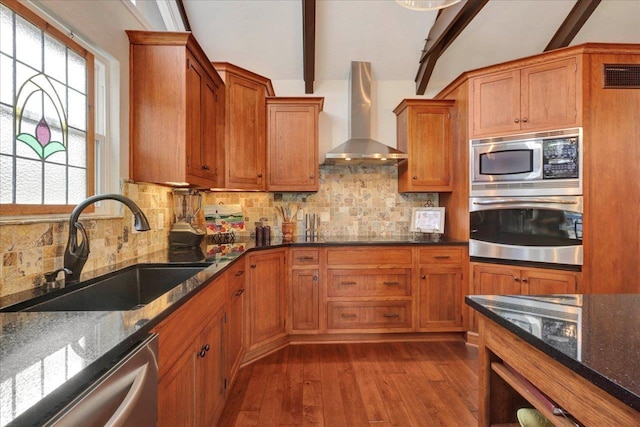 kitchen featuring visible vents, a sink, appliances with stainless steel finishes, wall chimney exhaust hood, and brown cabinetry