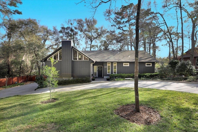 mid-century home featuring driveway, a chimney, a front yard, and fence