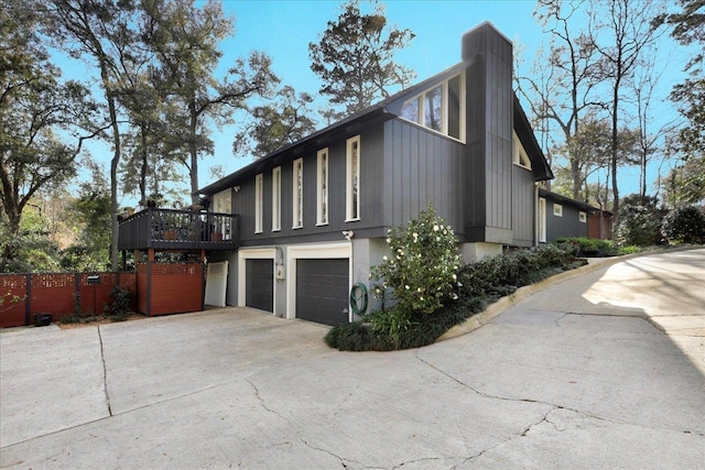 view of home's exterior with concrete driveway, fence, a garage, and a chimney