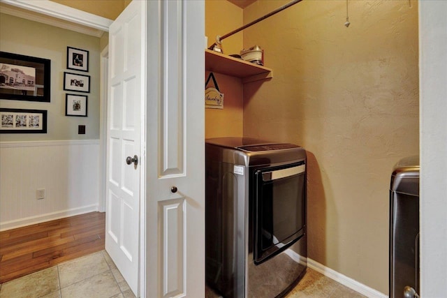 washroom with washer and dryer, laundry area, light tile patterned flooring, and a wainscoted wall