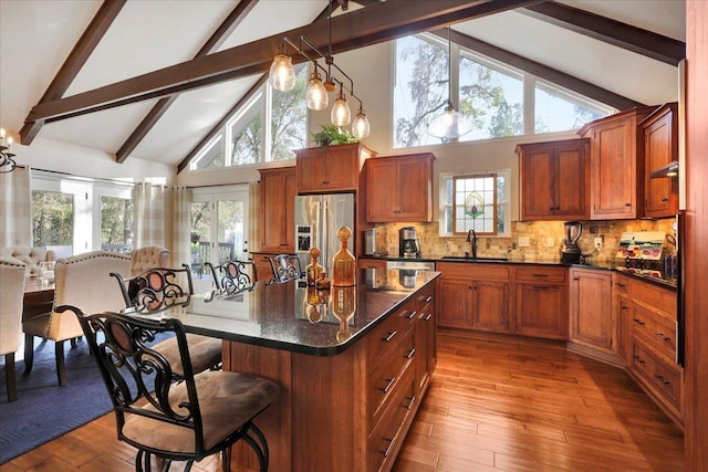 kitchen with a kitchen island, a kitchen breakfast bar, stainless steel refrigerator with ice dispenser, wood finished floors, and a sink