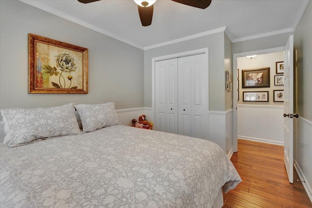 bedroom featuring crown molding, a wainscoted wall, wood finished floors, a closet, and a ceiling fan