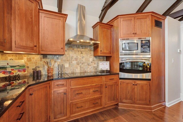 kitchen featuring visible vents, brown cabinets, appliances with stainless steel finishes, and wall chimney range hood