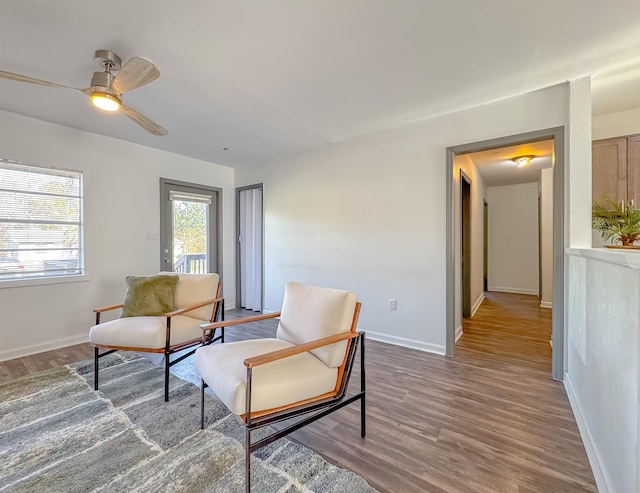 living area with a ceiling fan, wood finished floors, and baseboards