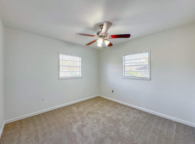 carpeted spare room featuring a wealth of natural light, a ceiling fan, and baseboards