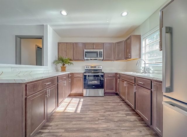 kitchen with light countertops, light wood-type flooring, appliances with stainless steel finishes, and a sink