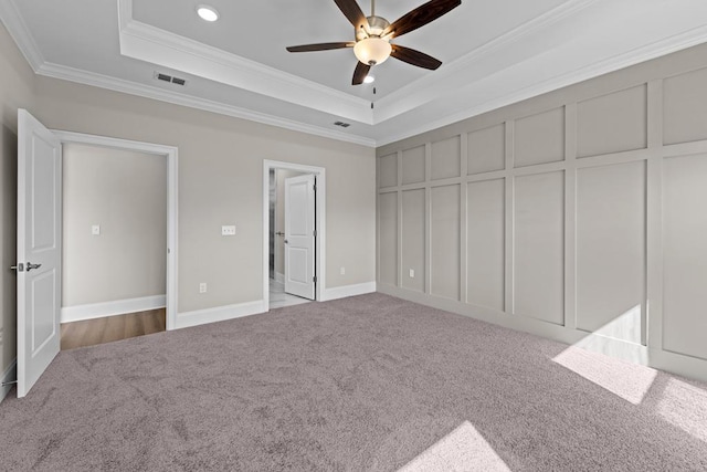 unfurnished bedroom featuring ceiling fan, light colored carpet, ornamental molding, and a raised ceiling