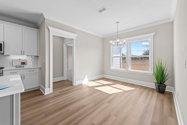 unfurnished dining area with an inviting chandelier, ornamental molding, and light hardwood / wood-style floors