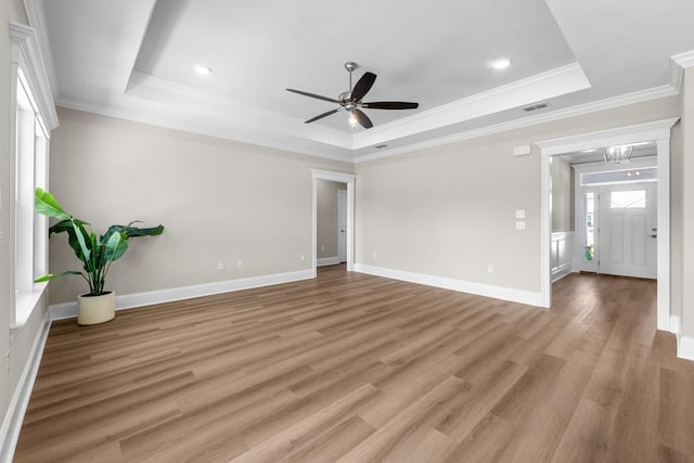 interior space with a tray ceiling, light hardwood / wood-style flooring, ornamental molding, and ceiling fan with notable chandelier