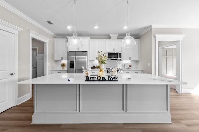 kitchen featuring appliances with stainless steel finishes, hardwood / wood-style floors, pendant lighting, white cabinets, and a large island with sink