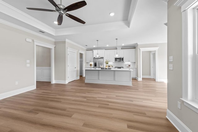 interior space featuring appliances with stainless steel finishes, a tray ceiling, hanging light fixtures, and a kitchen island