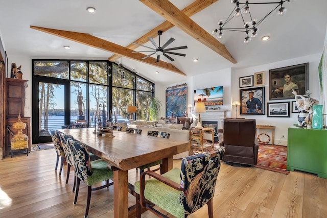 dining space with high vaulted ceiling, ceiling fan with notable chandelier, a water view, light hardwood / wood-style flooring, and beamed ceiling