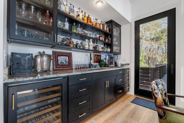 bar featuring light hardwood / wood-style floors, light stone countertops, sink, and wine cooler