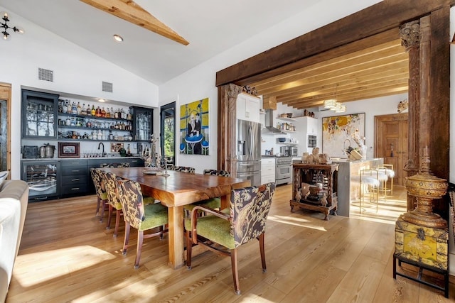 dining room featuring vaulted ceiling with beams, indoor bar, light hardwood / wood-style floors, and wine cooler