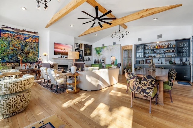 living room featuring ceiling fan, wet bar, beamed ceiling, high vaulted ceiling, and light wood-type flooring