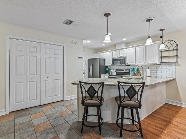 7214 Jaffrey Ct, Tallahassee, FL 32312 - kitchen with appliances with stainless steel finishes, a peninsula, white cabinetry, backsplash, and light stone counters
