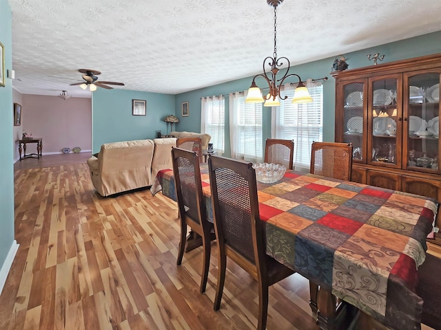 dining space with ceiling fan with notable chandelier, a textured ceiling, and light hardwood / wood-style flooring