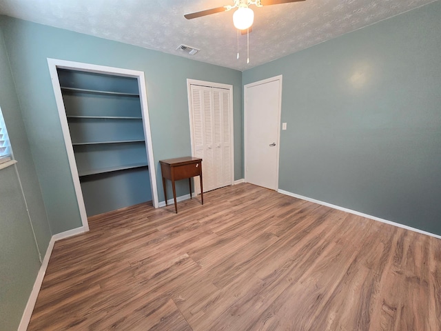 unfurnished bedroom featuring multiple closets, wood-type flooring, ceiling fan, and a textured ceiling