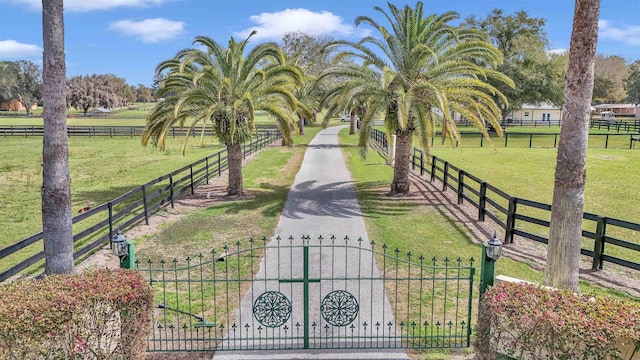 view of property's community with a rural view, a lawn, fence, and a gate