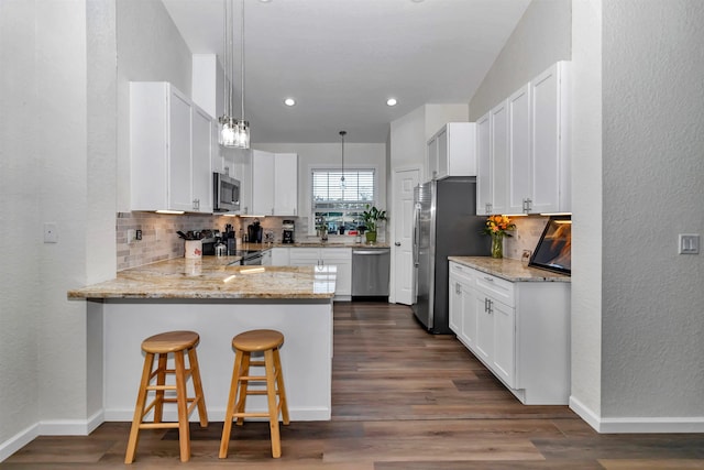 kitchen with stainless steel appliances, a peninsula, white cabinets, hanging light fixtures, and light stone countertops