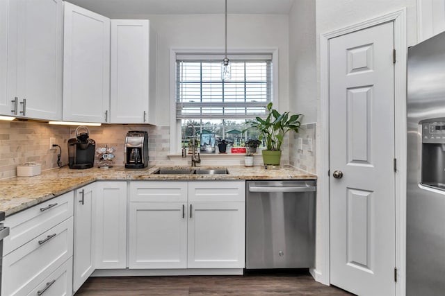 kitchen with hanging light fixtures, light stone countertops, stainless steel appliances, white cabinetry, and a sink