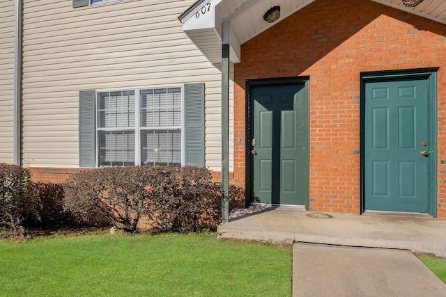 view of exterior entry featuring brick siding and a lawn