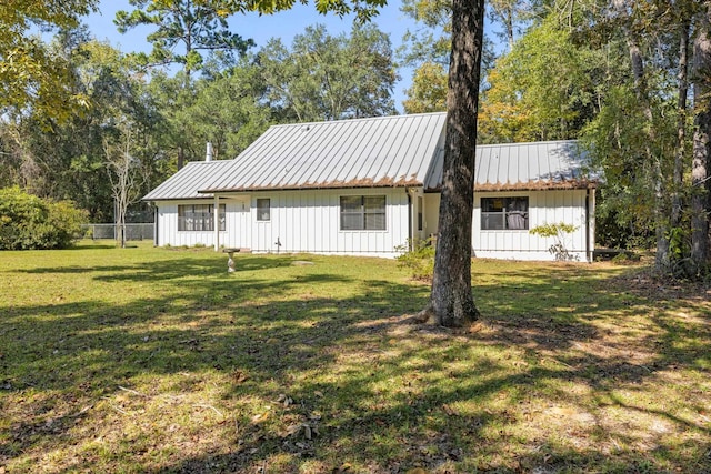 rear view of house featuring board and batten siding, a yard, metal roof, and fence