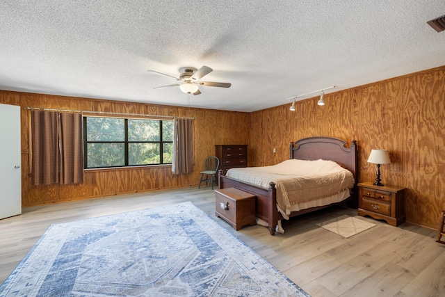 bedroom with track lighting, light wood-type flooring, and wooden walls