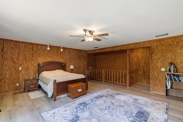 bedroom with light wood finished floors, wooden walls, rail lighting, visible vents, and a textured ceiling