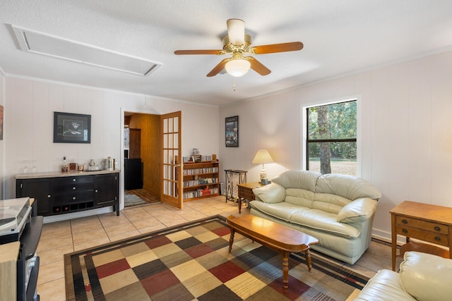 living area with attic access, a ceiling fan, crown molding, and light tile patterned floors