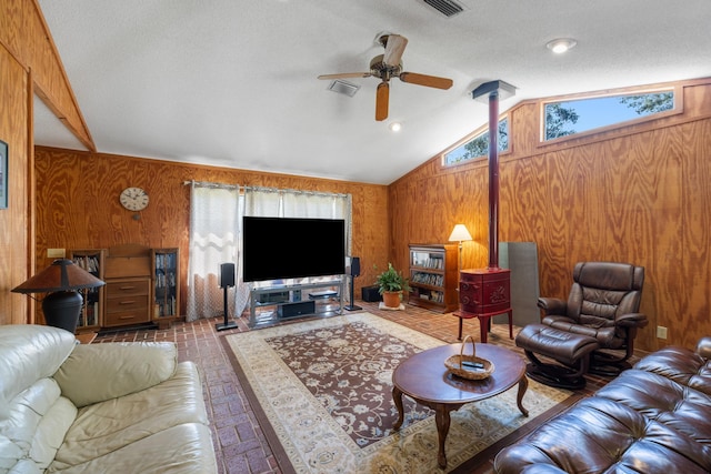 living room with visible vents, lofted ceiling, ceiling fan, wooden walls, and a wood stove