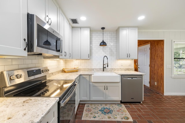 kitchen featuring stainless steel appliances, a sink, tasteful backsplash, visible vents, and brick floor