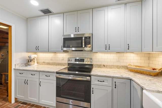 kitchen featuring visible vents, white cabinetry, backsplash, brick floor, and appliances with stainless steel finishes