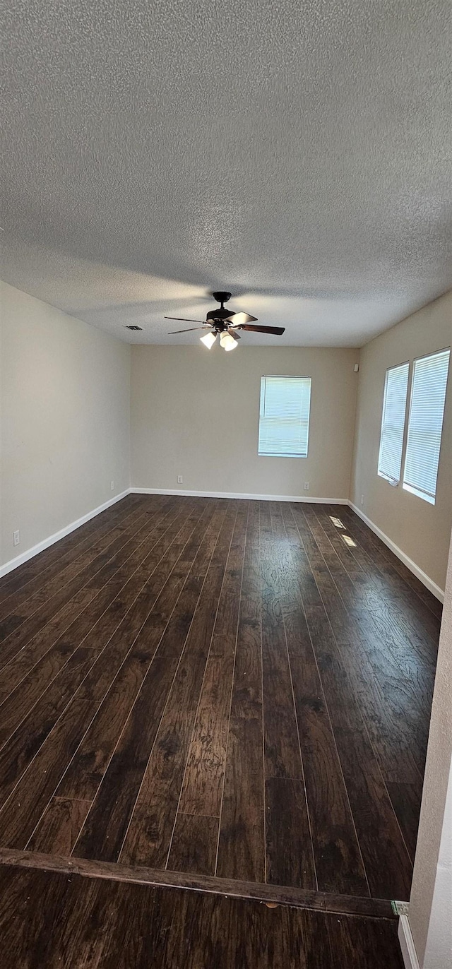 spare room featuring a ceiling fan, a textured ceiling, baseboards, and dark wood finished floors