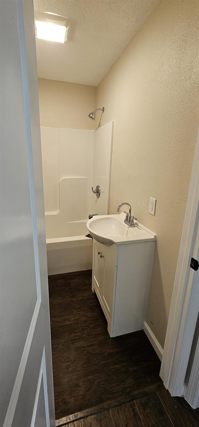 bathroom featuring a textured ceiling, wood finished floors, vanity, shower / washtub combination, and a textured wall