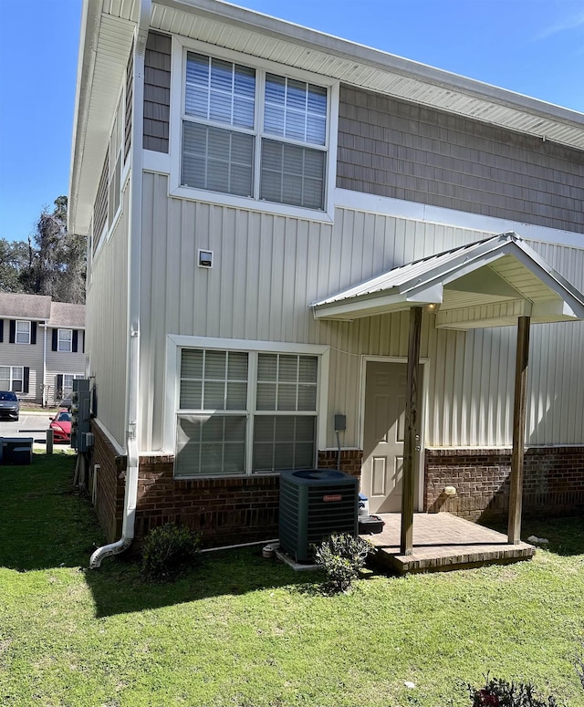 rear view of property featuring cooling unit, brick siding, and a lawn