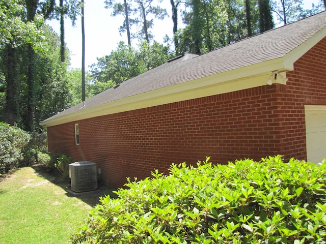 view of home's exterior featuring central air condition unit, a lawn, a garage, brick siding, and roof with shingles