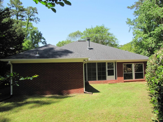 rear view of house with a lawn, brick siding, and roof with shingles