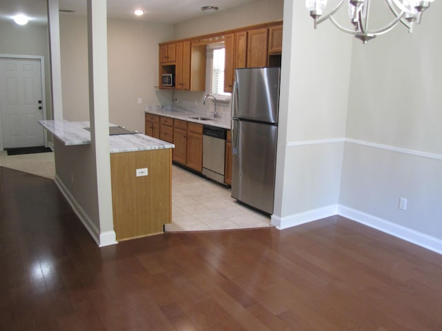 kitchen featuring an inviting chandelier, a sink, light wood-type flooring, brown cabinetry, and appliances with stainless steel finishes