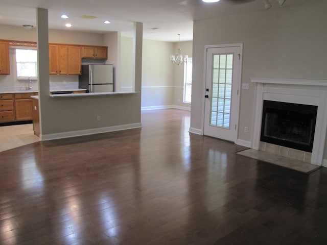unfurnished living room with a fireplace with flush hearth, recessed lighting, an inviting chandelier, wood finished floors, and a sink