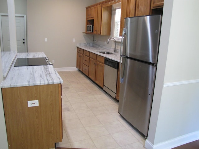 kitchen featuring light stone counters, a sink, brown cabinetry, baseboards, and appliances with stainless steel finishes