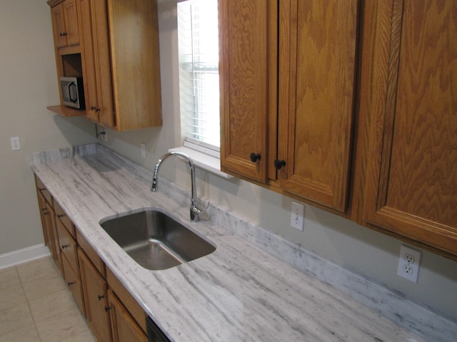 kitchen featuring a sink, stainless steel microwave, light stone countertops, baseboards, and brown cabinetry