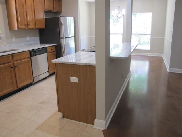 kitchen featuring stainless steel appliances, a sink, baseboards, an inviting chandelier, and brown cabinets