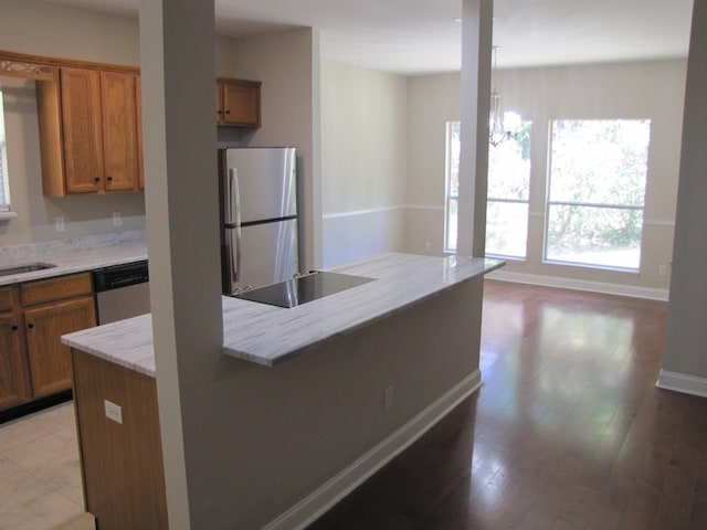 kitchen featuring baseboards, light stone counters, brown cabinetry, and appliances with stainless steel finishes