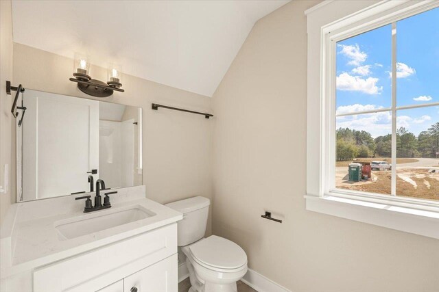 bathroom featuring plenty of natural light, vanity, vaulted ceiling, and toilet