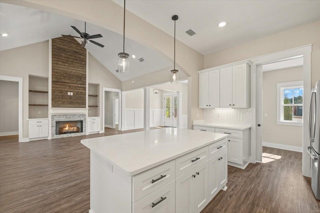 kitchen with white cabinets, decorative backsplash, a kitchen island, and a stone fireplace