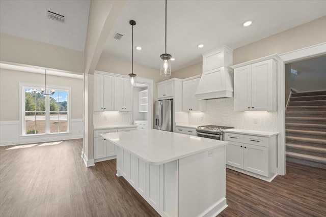 kitchen featuring appliances with stainless steel finishes, premium range hood, white cabinetry, and pendant lighting